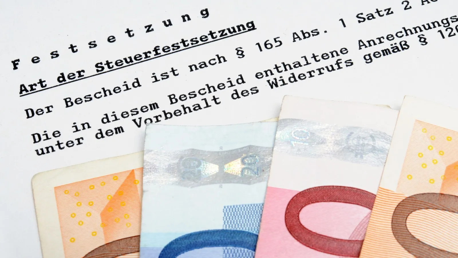 Deutscher Steuerbescheid und nah aufgenommenen Euro-Scheinen, die darauf liegen.